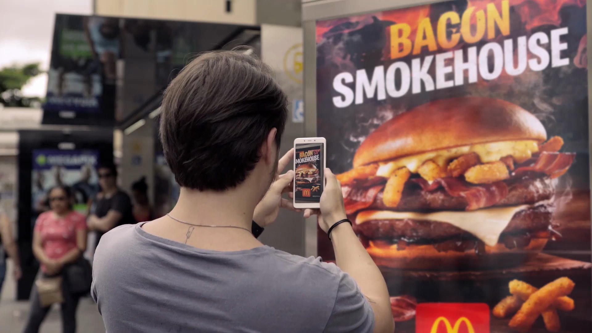A person on a street pointing a phone at a rival poster, which is burning inside the screen