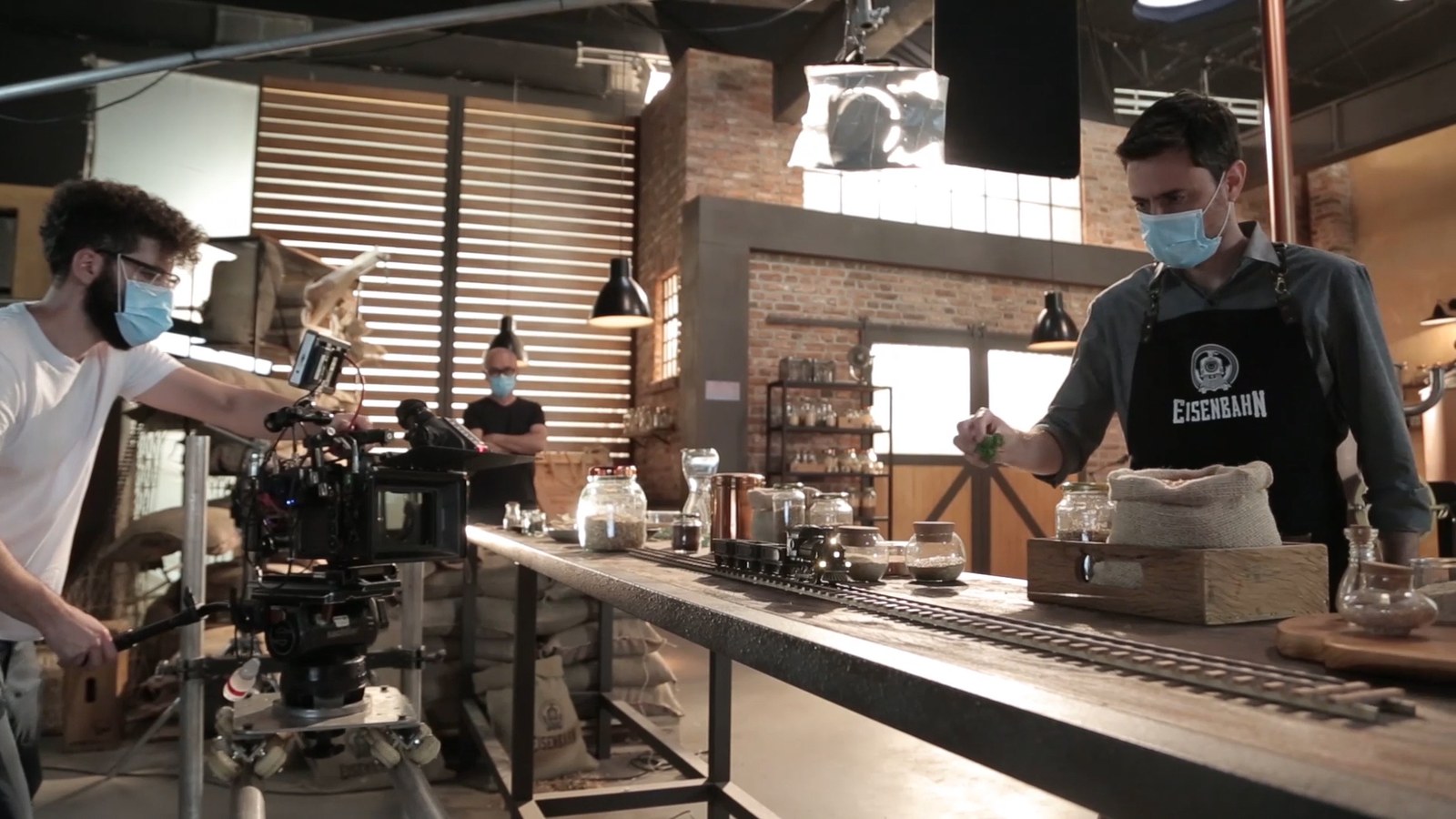 Crew in masks around the miniature brewery set with a camera rig