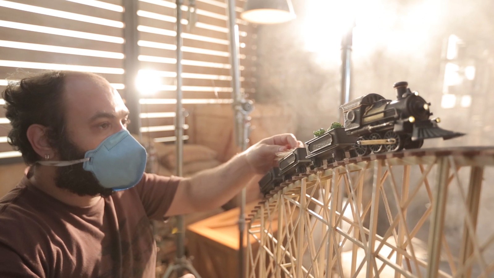 A crew member in a mask placing the model train on the wheat set