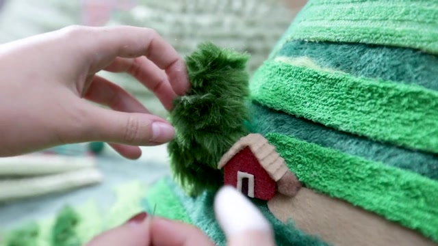 A hand places a tiny red house on a knitted green hillside, behind the scenes of Nescafe Reserva Mexicana