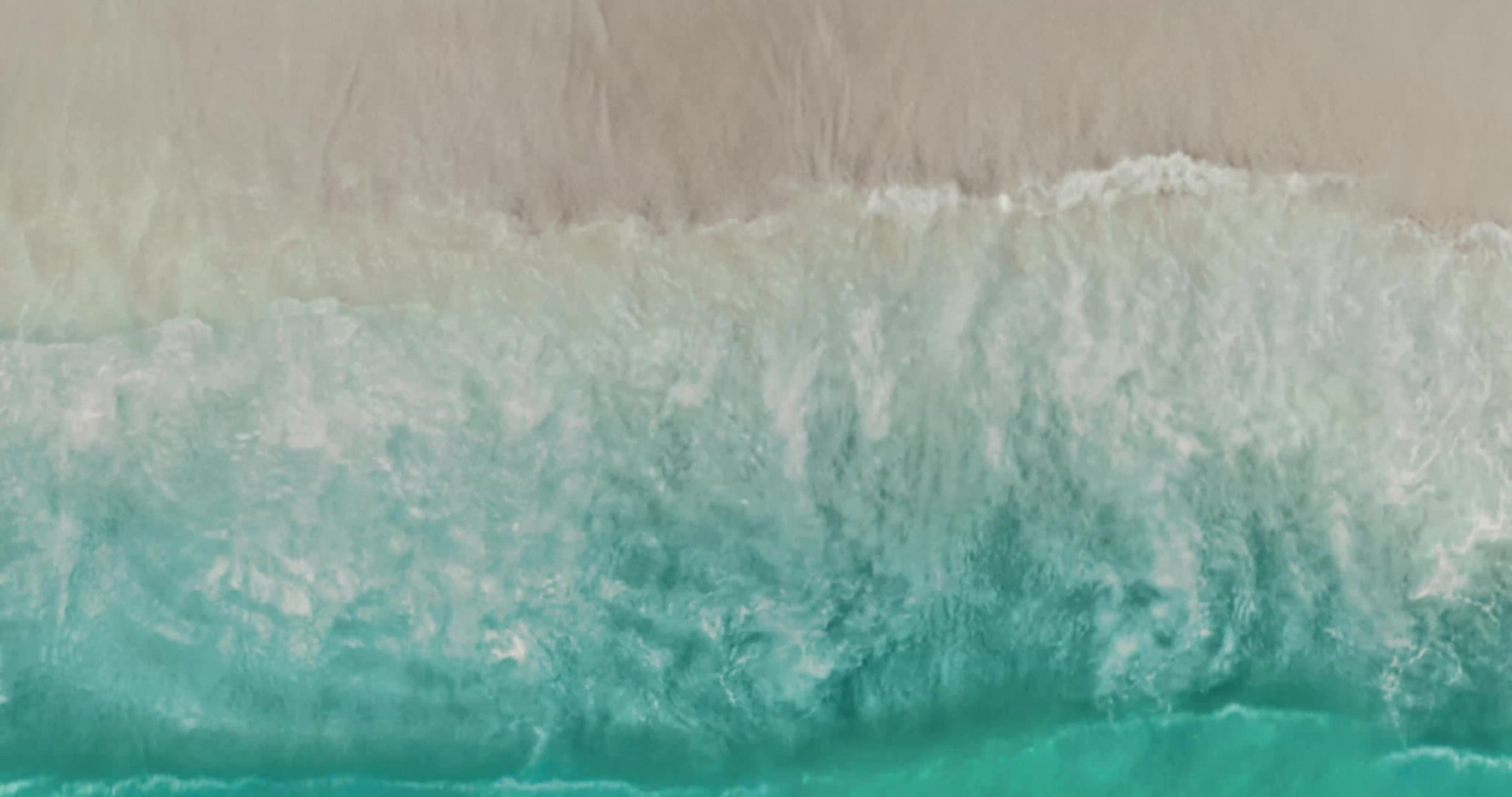 Aerial frame of real ocean surf breaking on sand