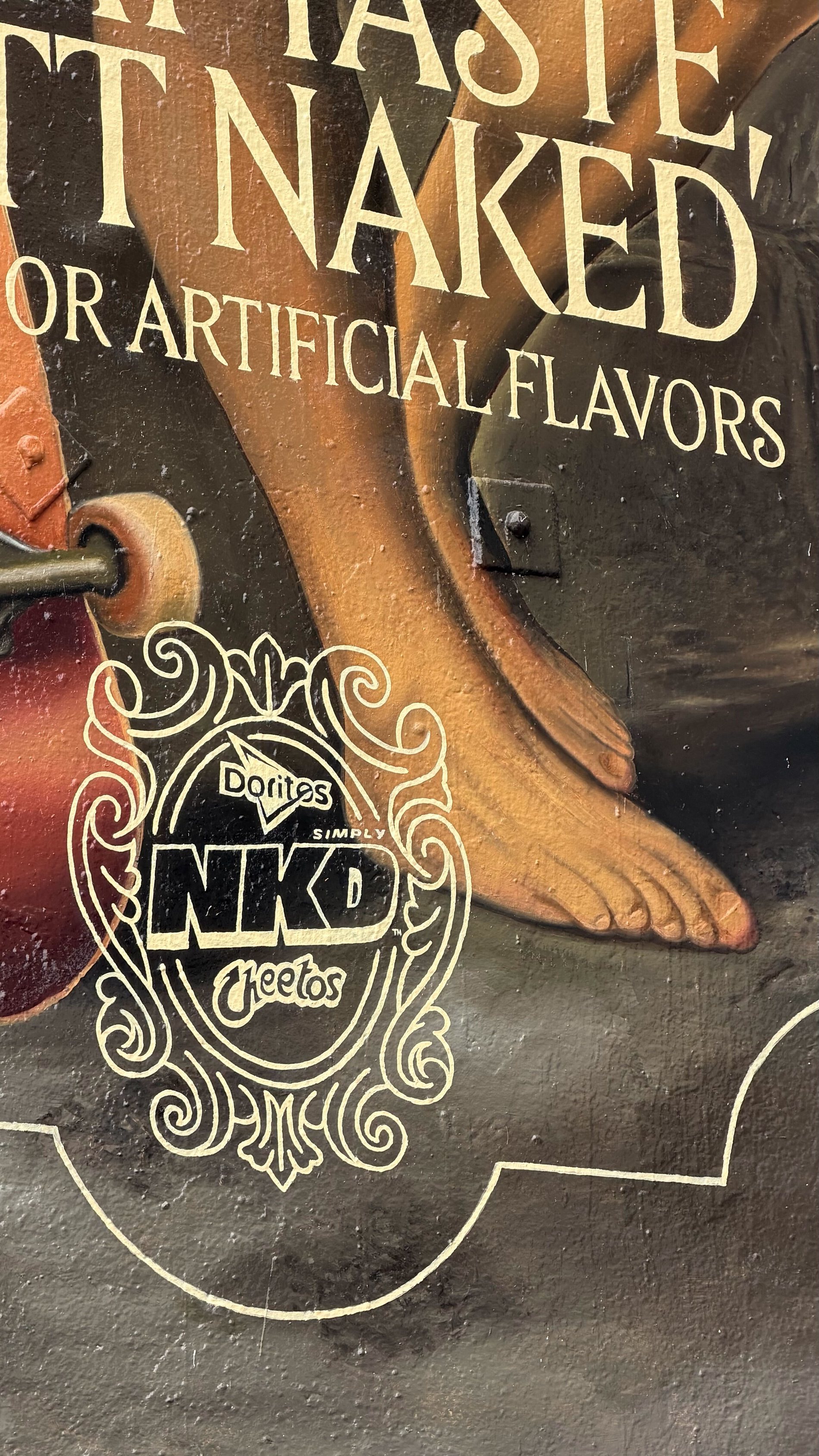 Detail of the lower mural, bare feet on a skateboard beside the Simply NKD mark
